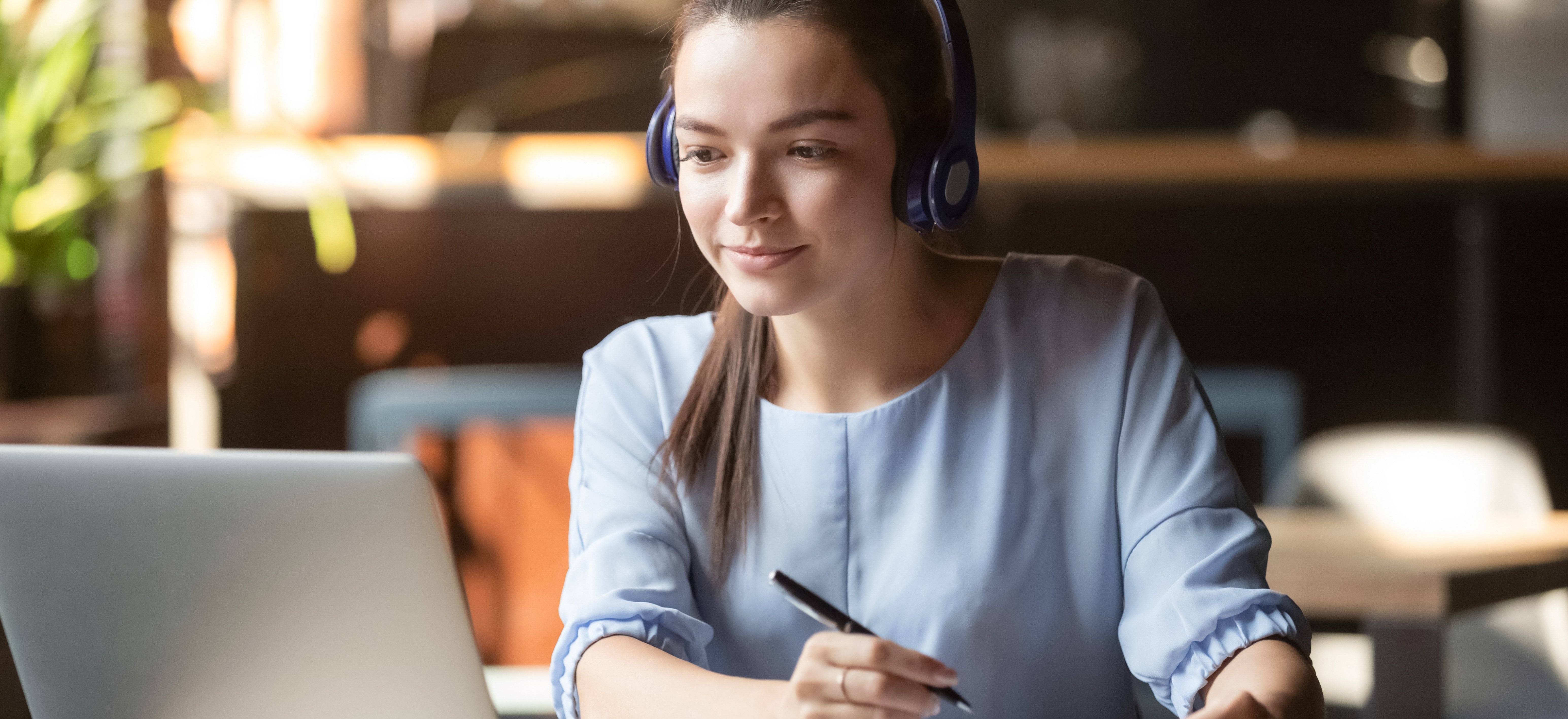 Junge Frau mit Kopfhörer schaut konzentriert auf Laptop